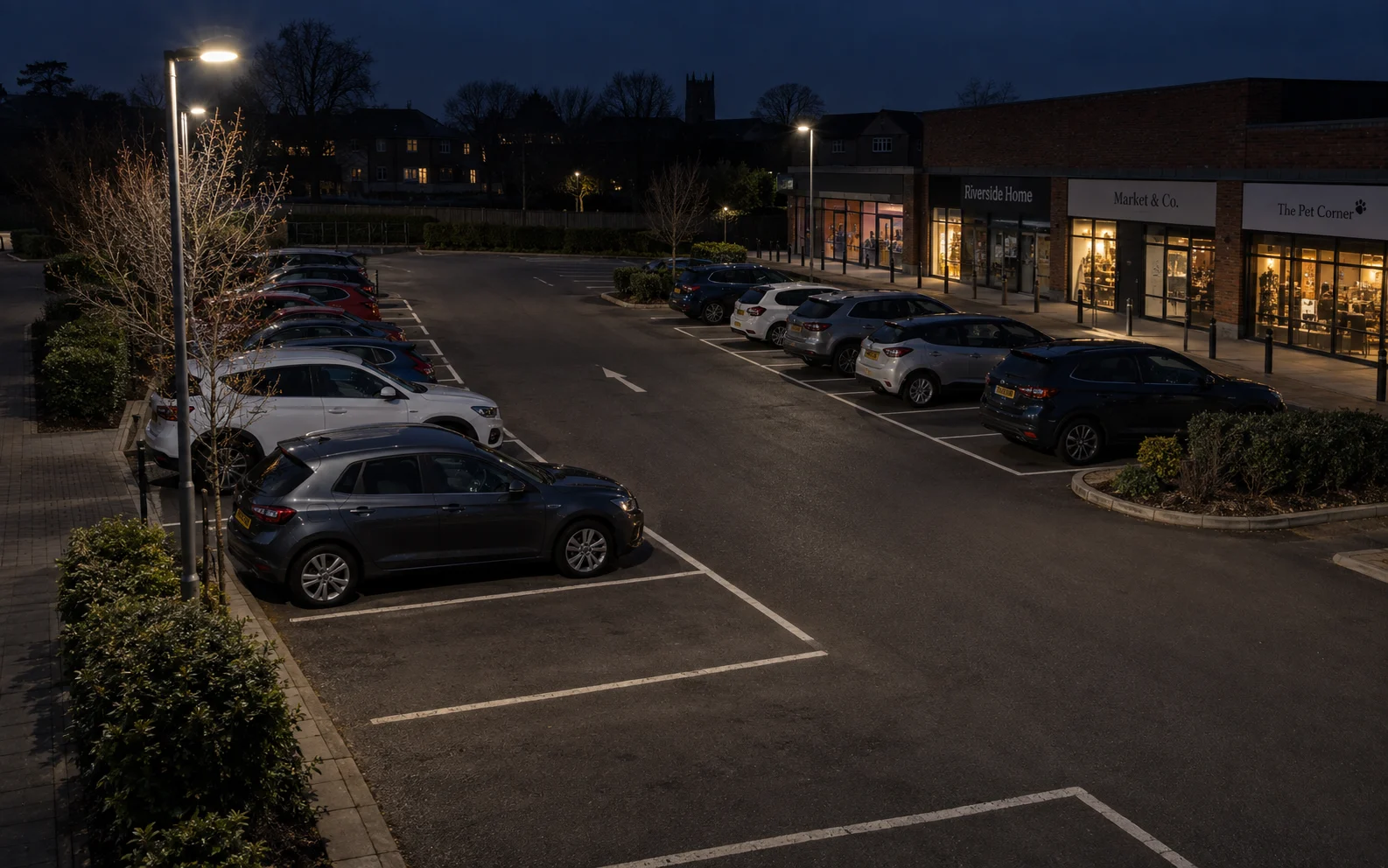 Elevated evening view of parking spaces, pedestrian paths and shop entrances.