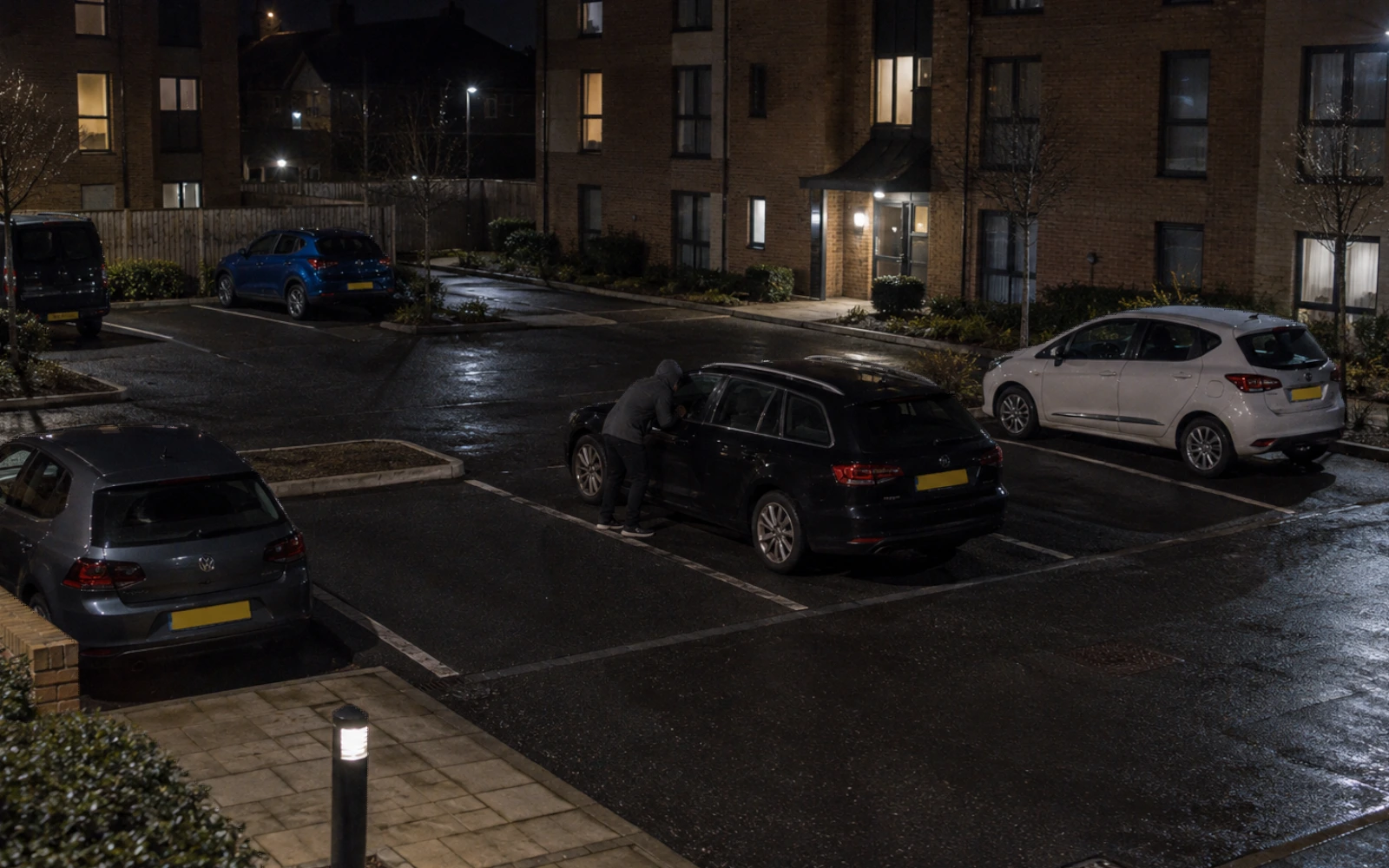 Night-time camera view of a person beside a stationary car on a residential site.