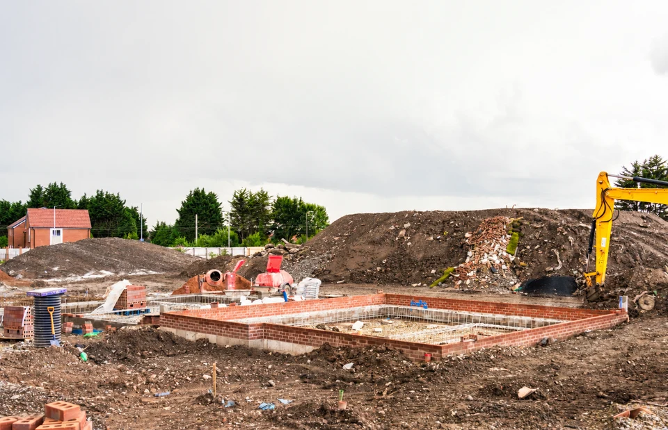Foundations, building materials and an excavator on a housing construction site.