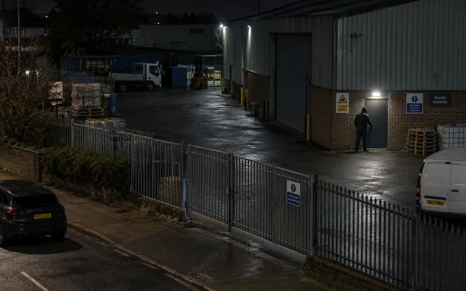 An elevated night-time view of a person near a warehouse door and storage yard.