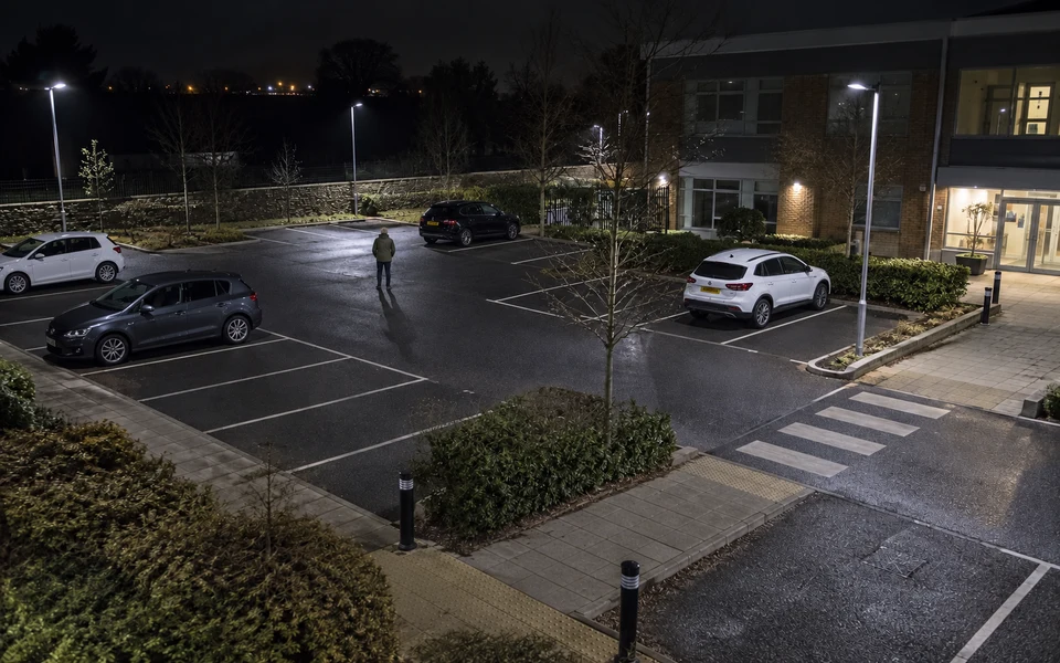 An elevated night-time view of a person approaching parked cars outside an office.
