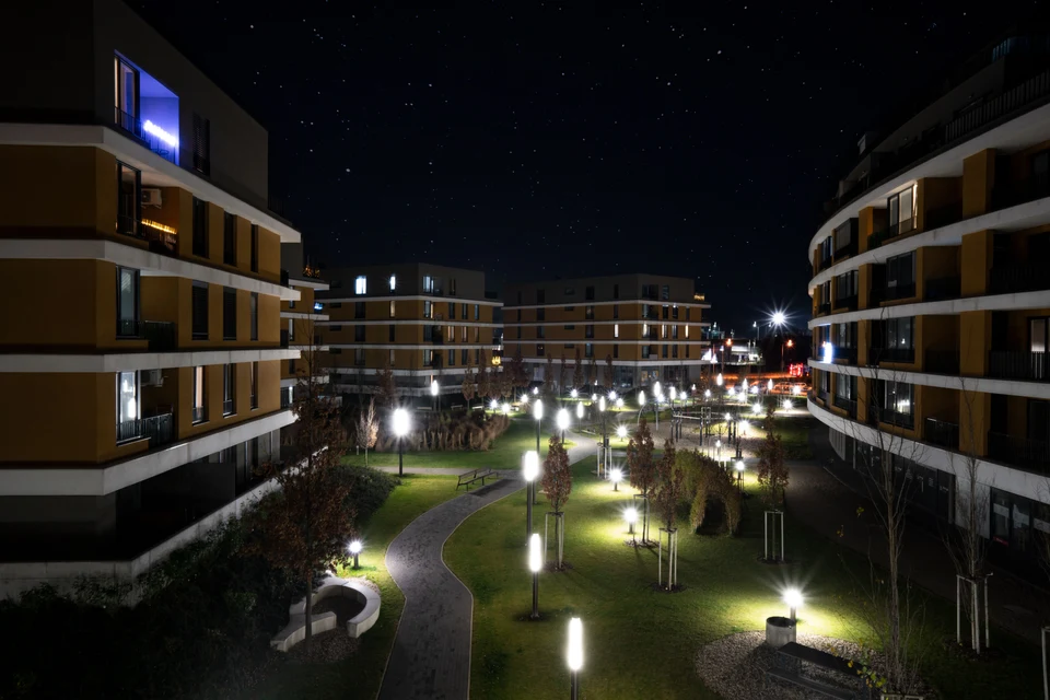 Illuminated outdoor paths and gardens between apartment buildings at night.