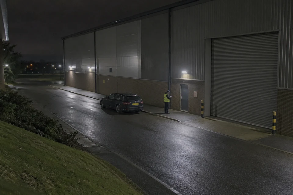 A security officer checking a warehouse entrance at night.