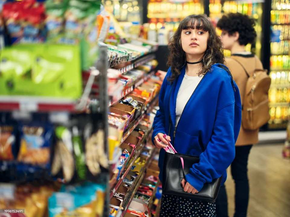 A woman in a blue hoodie with a black handbag beside shop shelves.