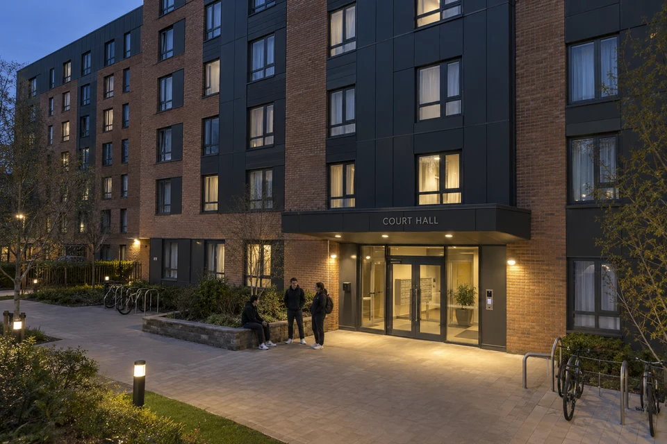 Three adults gathered outside the entrance of a purpose-built student residence at dusk.